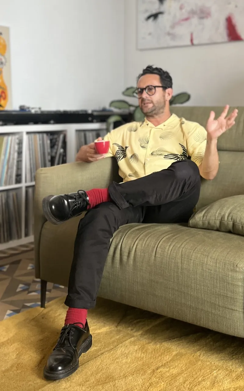 Maurice Aymard sentado en un sofá, hablando con una taza de café en la mano